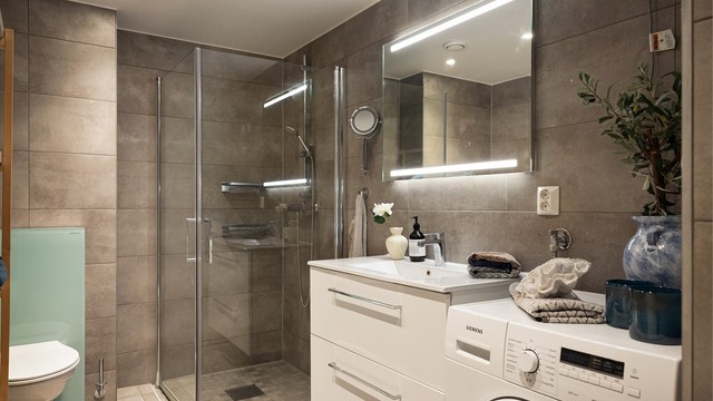 Badet holder en moderne standard med flislagte overflater, vannbåren gulvvarme og praktisk opplegg for vaskemaskin.