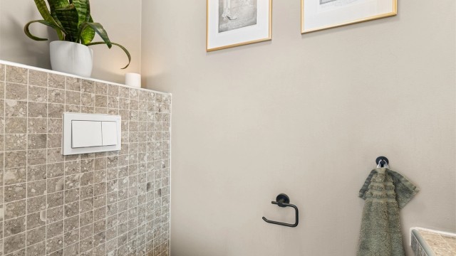 Rommet er innredet med vegghengt toalett og en flislagt benkeplate med ovenpåliggende servant.