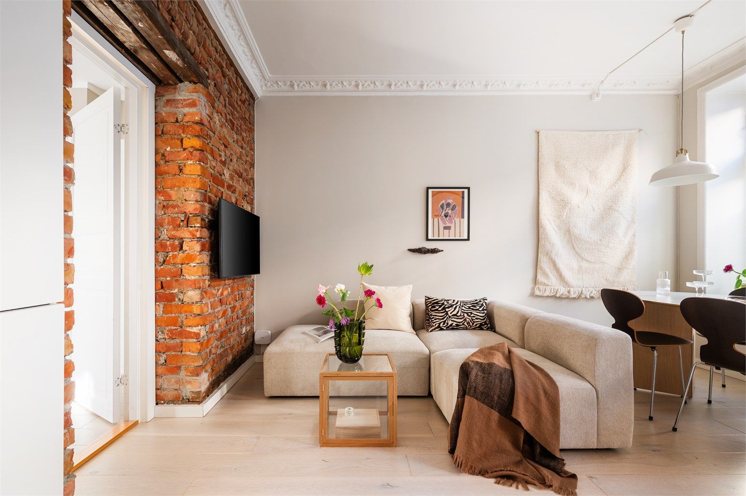 En eksponert teglsteinsvegg gir stuen en rustikk og stilig kontrast til de ellers moderne overflatene.