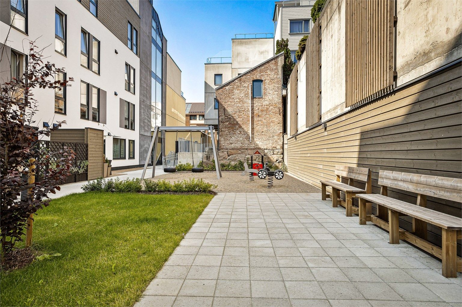 Leiligheten har tilgang til hyggelig bakgård med felles sykkelparkering samt lekeplass med lekeapparater - Sommerbilde fra tidligere annonse.
