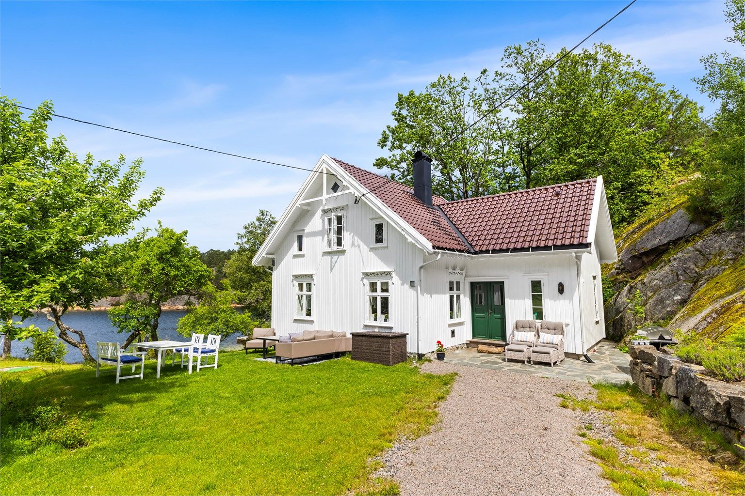 Det hvite hovedhuset er nylig renovert og tilbygget, og fremstår friskt og innbydende. Utenfor er det koselig hage med gamle frukttrær og nydelig utsikt mot vannet.  