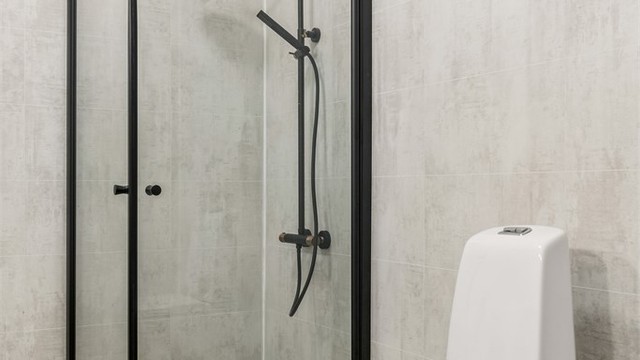 Badet har stilig gulvbelegg med gulvvarme, baderomsplater på veggene og innredning med servant, speil og dusjhjørne.