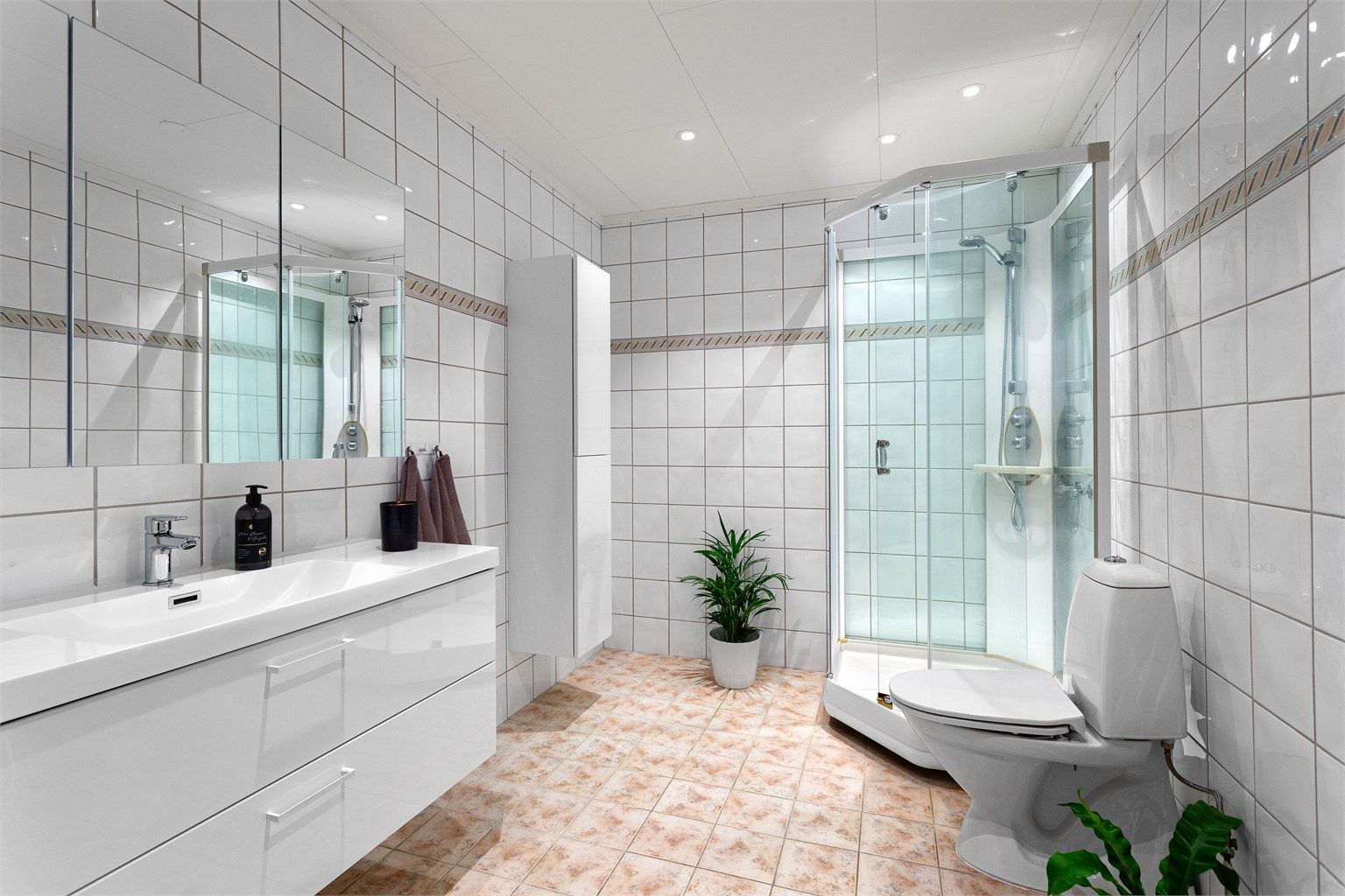 Flislagt bad med gulvvarme. Downlights i himlingen. Innredet med vegghengt servantskap med skuffer. Speilskap på vegg over servant.