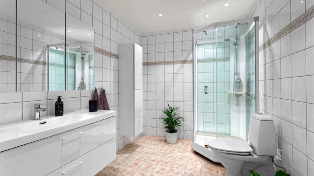 Flislagt bad med gulvvarme. Downlights i himlingen. Innredet med vegghengt servantskap med skuffer. Speilskap på vegg over servant.