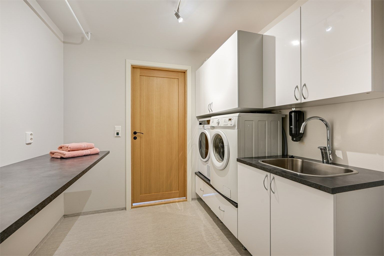 Praktisk vaskerom med opplegg til vaskemaskin og tørketrommel i tilpasset vaskeromsinnredning, samt innredning med nedfelt utslagsvask av stål.