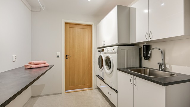 Praktisk vaskerom med opplegg til vaskemaskin og tørketrommel i tilpasset vaskeromsinnredning, samt innredning med nedfelt utslagsvask av stål.