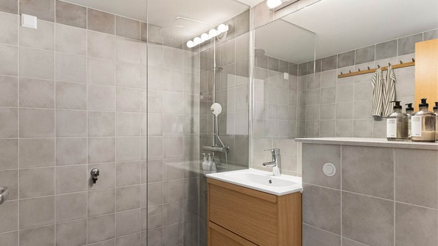 Badet i 7. etasje er helflislagt med elektrisk gulvvarme, vegghengt toalett og dusjhjørne i glass og har et et rent og gjennomført uttrykk.