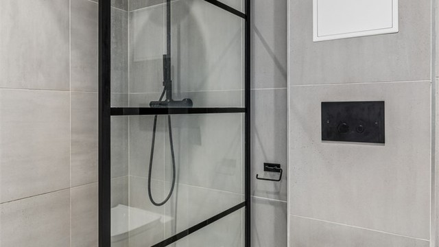 Dusjnisje med glassvegg, veggmontert klosett og innfelte downlights i himlingen.