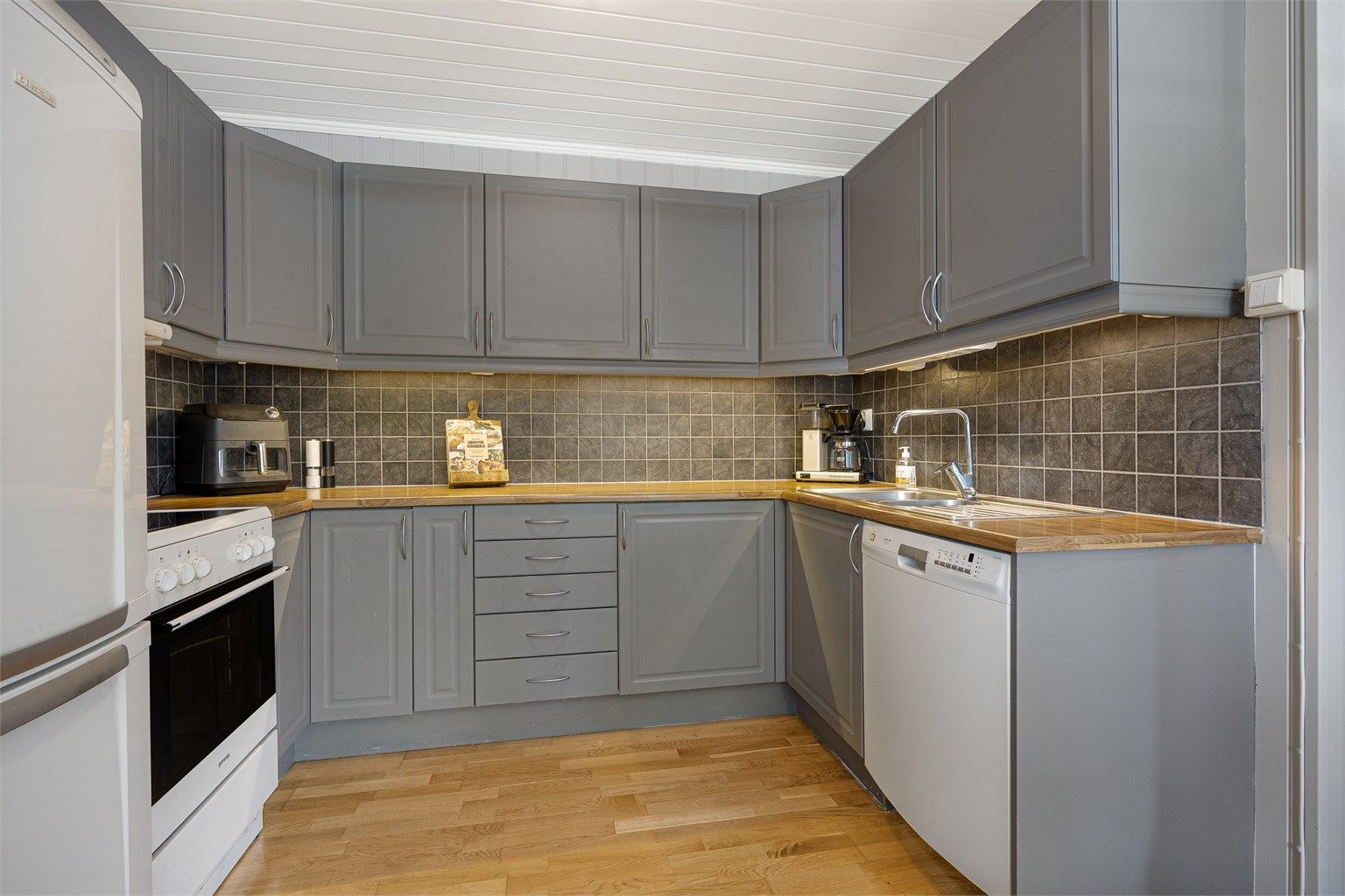 Kjøkkeninnredning fra Sigdal med malte, glatte fronter og laminat benkeplate. Det er opplegg for frittstående hvitevarer.