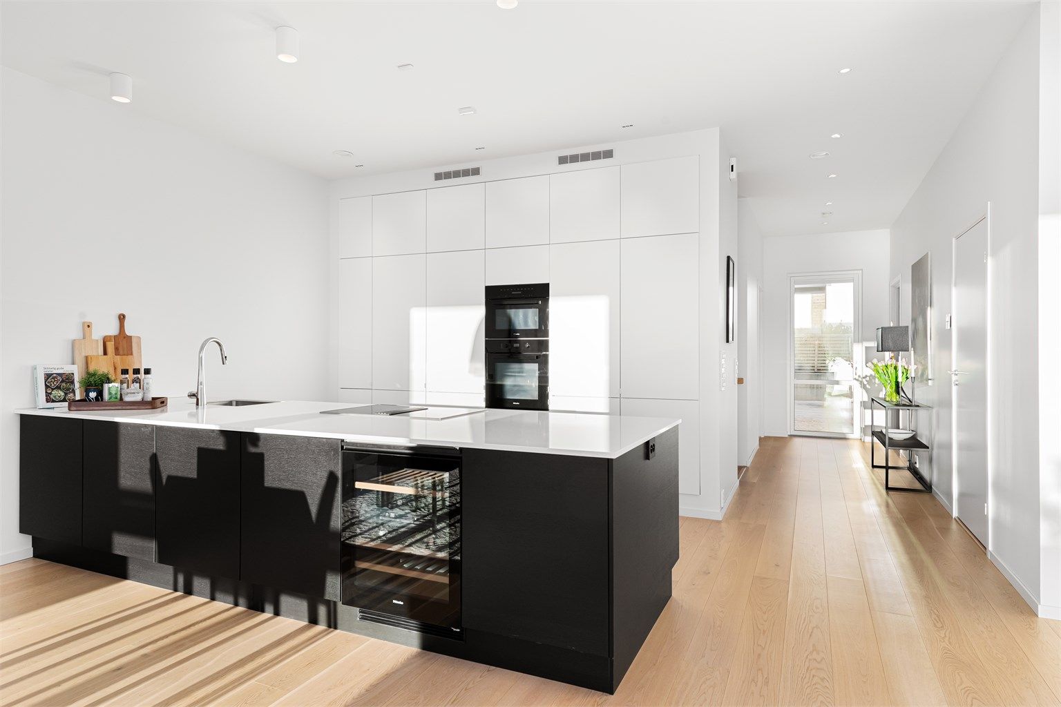 Kjøkkeninnredning fra HTH med hvite fronter på høyskap og mørke glatte fronter på kjøkkenøy. Benkeplate av stein