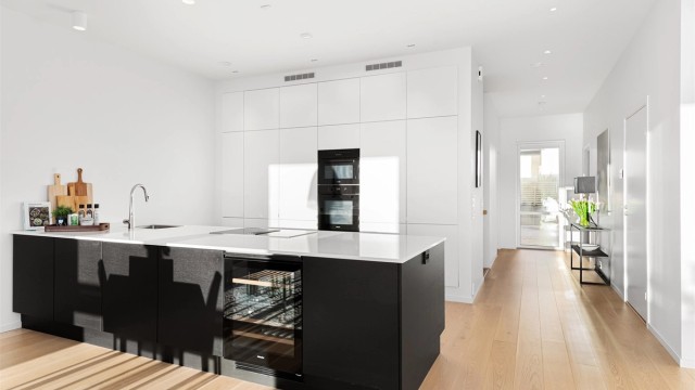 Kjøkkeninnredning fra HTH med hvite fronter på høyskap og mørke glatte fronter på kjøkkenøy. Benkeplate av stein