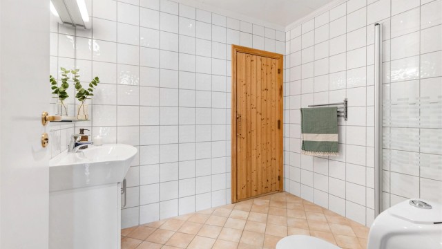 Speil med hylle av glass samt belysning med stikkontakt på vegg over servant. Dusjsone med innfellbare dører av glass. Dusjarmatur tilkoblet hånddusj. Gulvstående toalett. Mekanisk avtrekksventil i himling.
