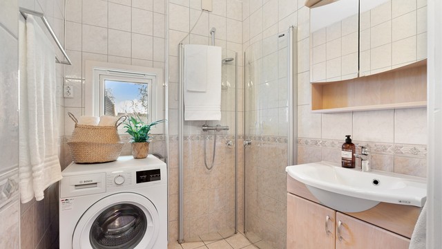 Pent flislagt bad med servantskap med speil og lys, opplegg for vaskemaskin og dusjhjørne.