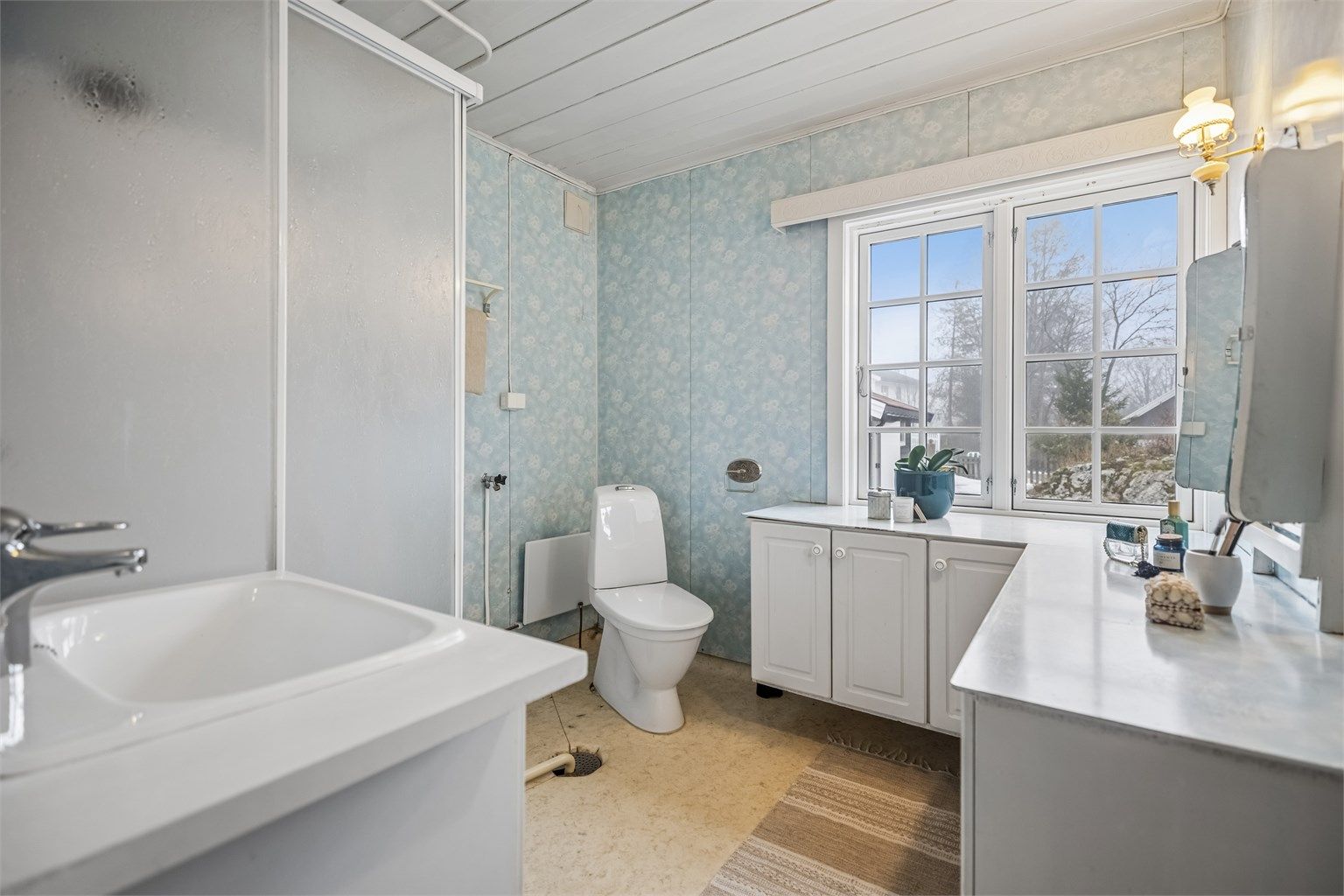 Eldre bad med dusjkabinett, servantinnredning, gulvstående toalett og opplegg for vaskemaskin.