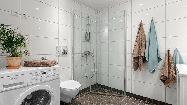 Badet er innredet med servantskap med speil og sideskap, dusjhjørne og vegghengt toalett .