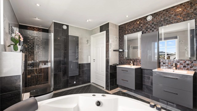 Badet har også separat dusjsone og toalett, mens innfelte downlights og dekorative flisdetaljer gir et helhetlig uttrykk.