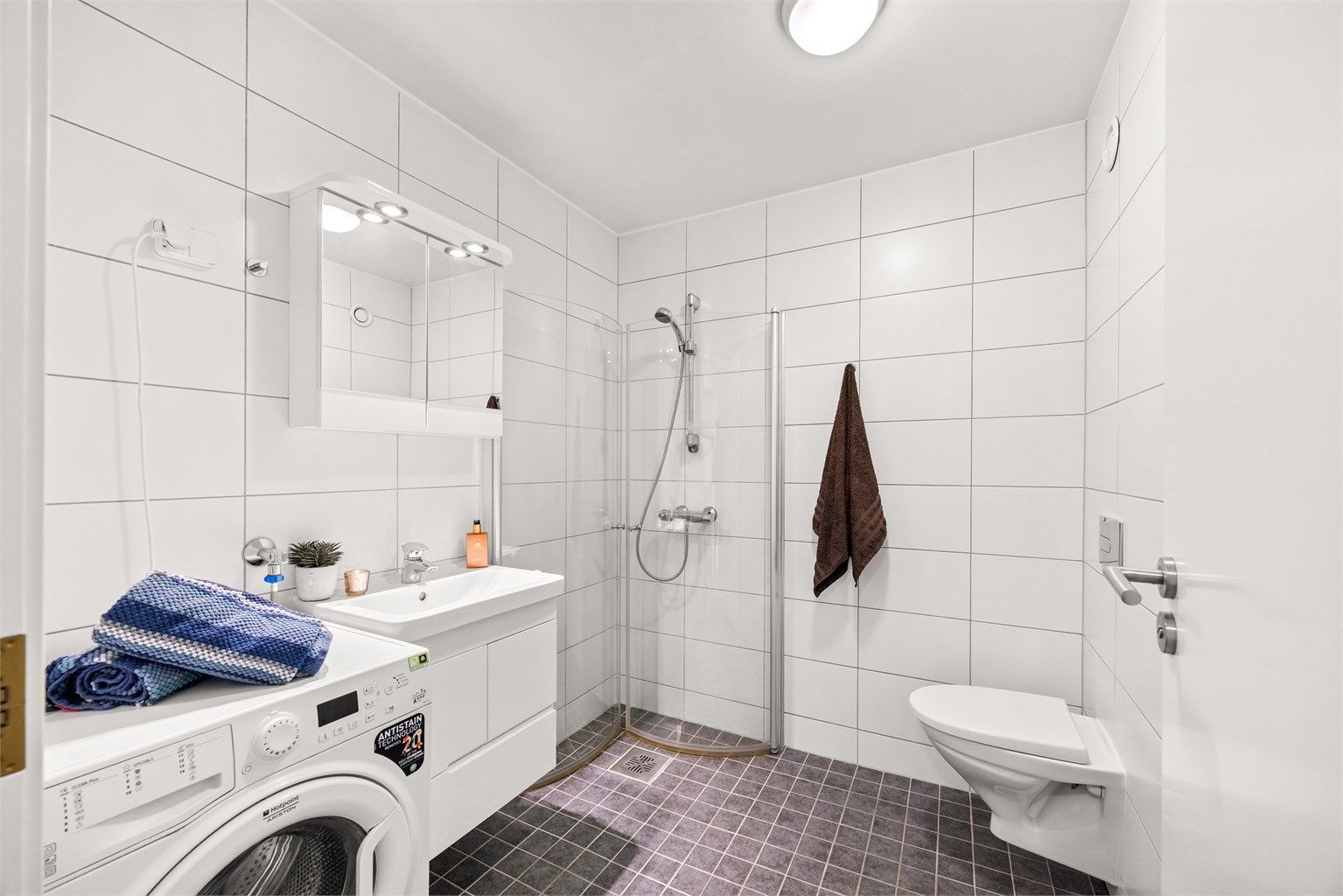 Badet er innredet med vegghengt toalett, dusjhjørne og servantinnredning.