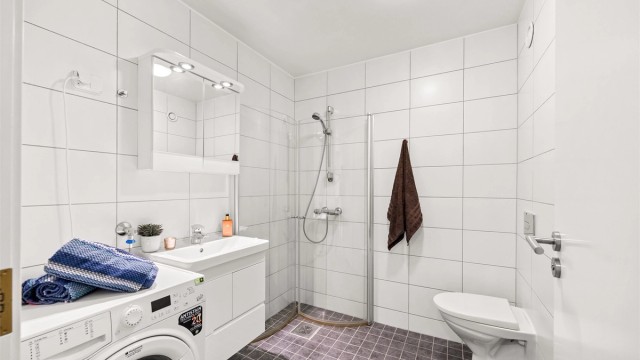 Badet er innredet med vegghengt toalett, dusjhjørne og servantinnredning.