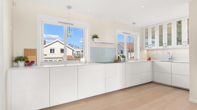 Kjøkkenet fremstår som en velutstyrt, funksjonell og innbydende arbeidsplass, i direkte tilknytning til stue og spisestue. Store vindusflater sørger for rikelig med naturlig lys. Innredningen har glatte fronter og en solid benkeplate i kompositt.