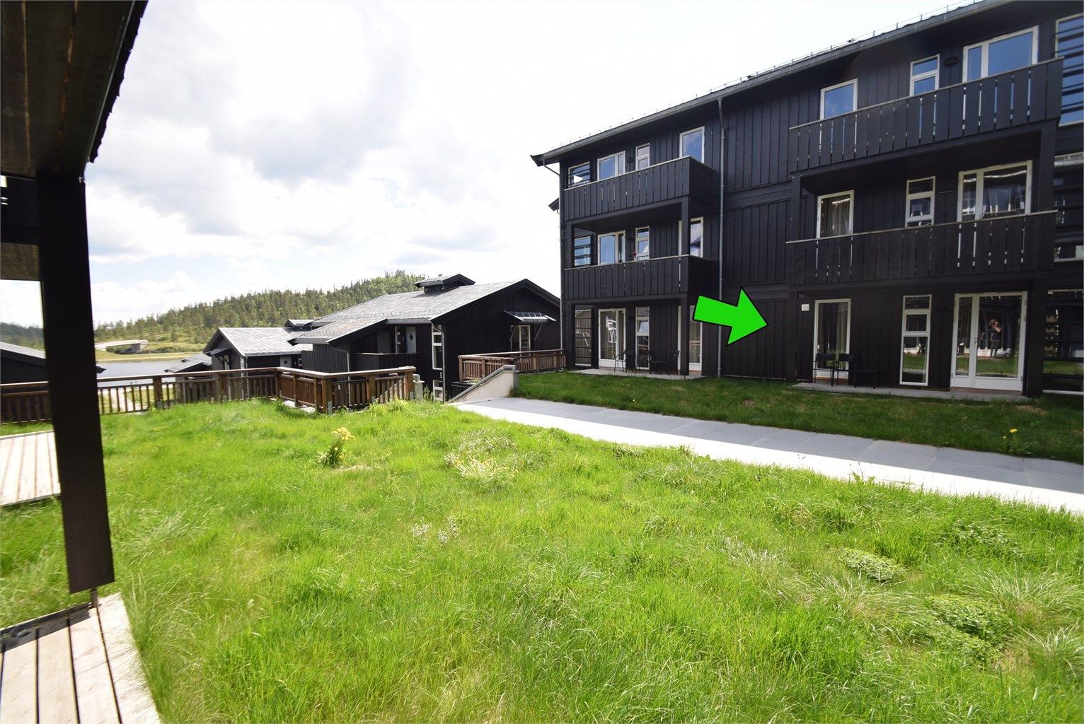 Leiligheten ligger tilbaketrukket fra gangstien med plen i front.