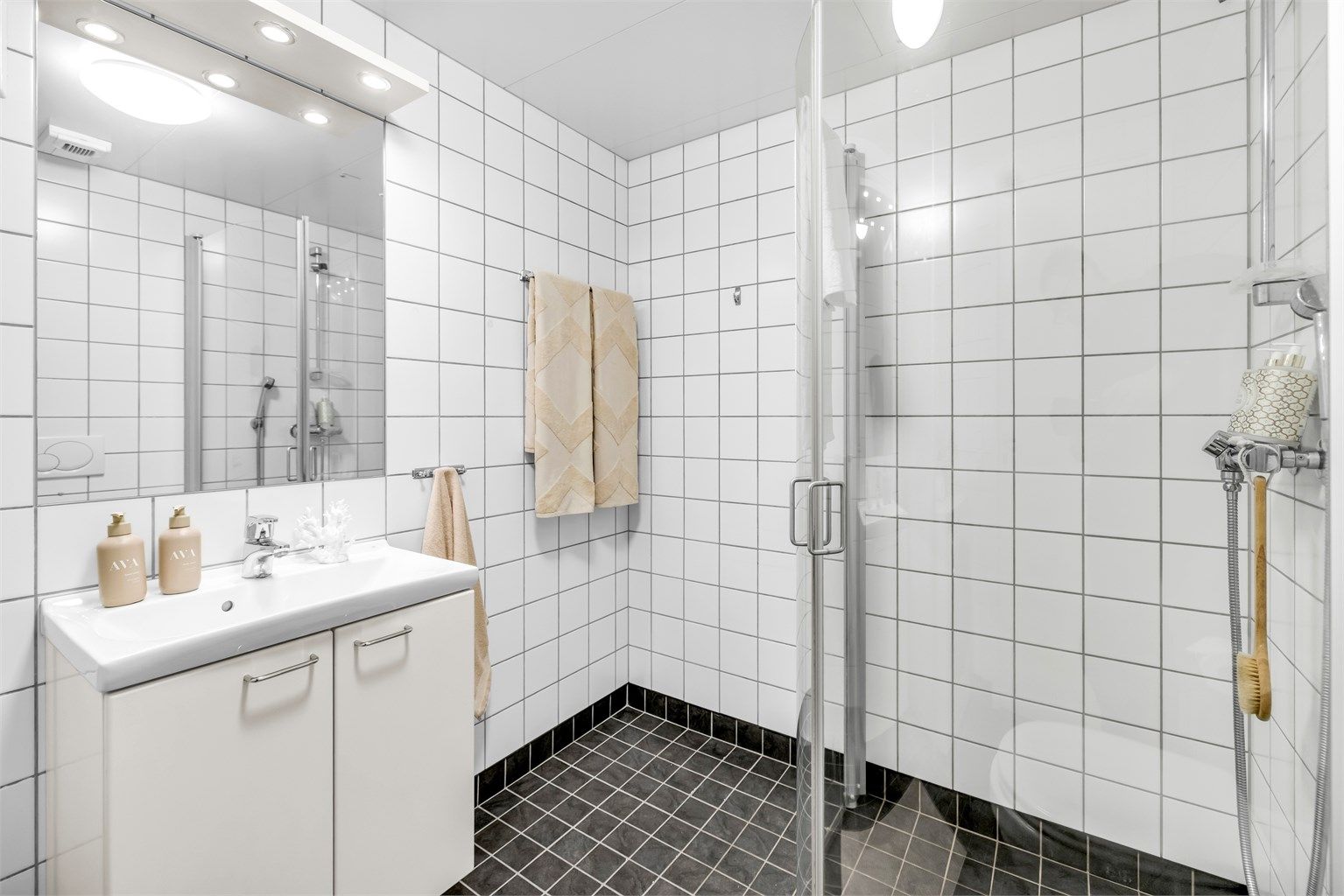 Badet er innredet med vegghengt toalett og servantinnredning med ovenpåliggende vask og speilskap med lys og stikkontakt over vasken.