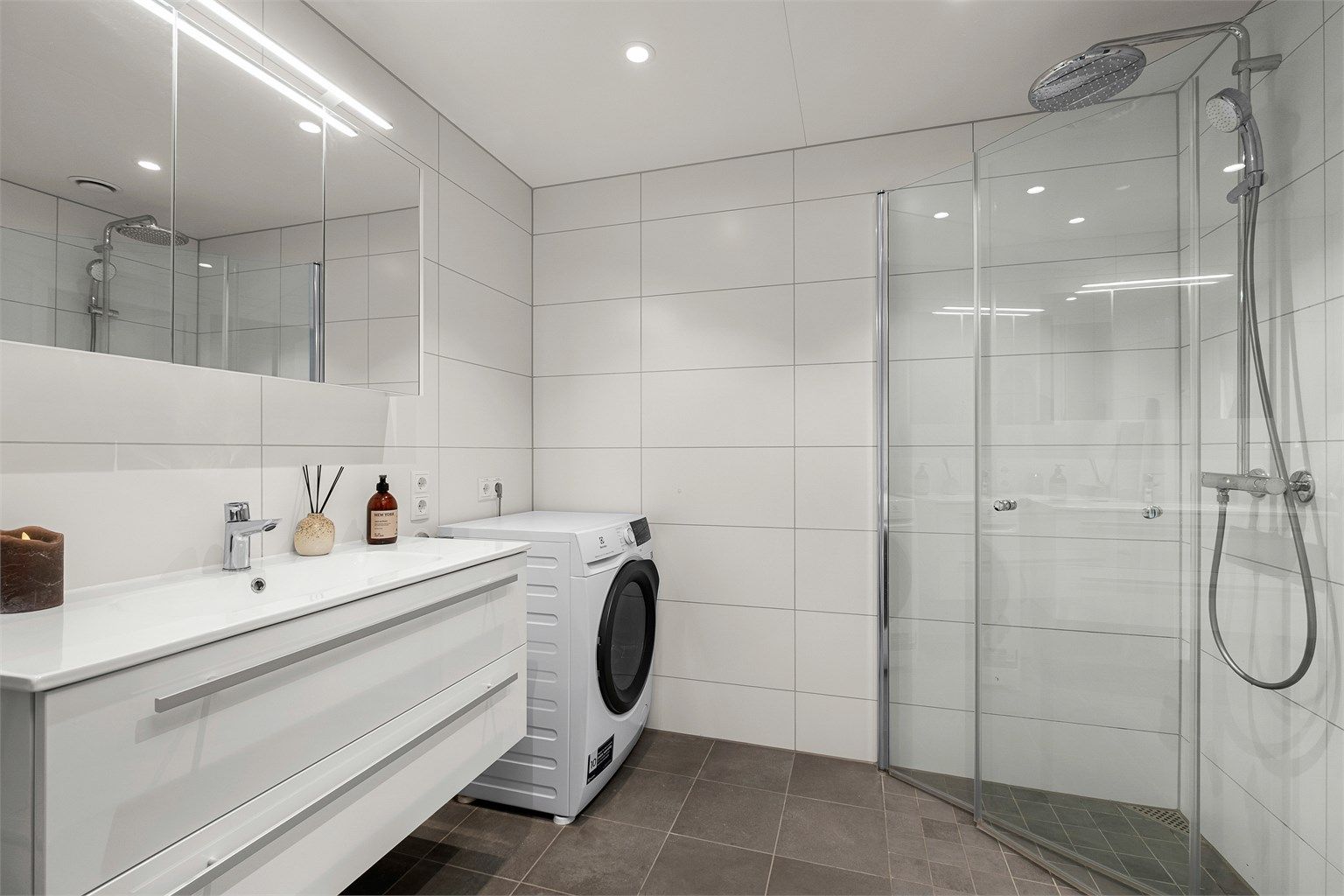 Pent flislagt bad på 5 kvm med gulvvarme, downlights i himling og opplegg for vaskemaskin. Videre er badet innredet med servantskap med speil og lys, dusjhjørne med regndusj og vegghengt toalett. 