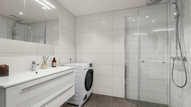 Pent flislagt bad på 5 kvm med gulvvarme, downlights i himling og opplegg for vaskemaskin. Videre er badet innredet med servantskap med speil og lys, dusjhjørne med regndusj og vegghengt toalett.