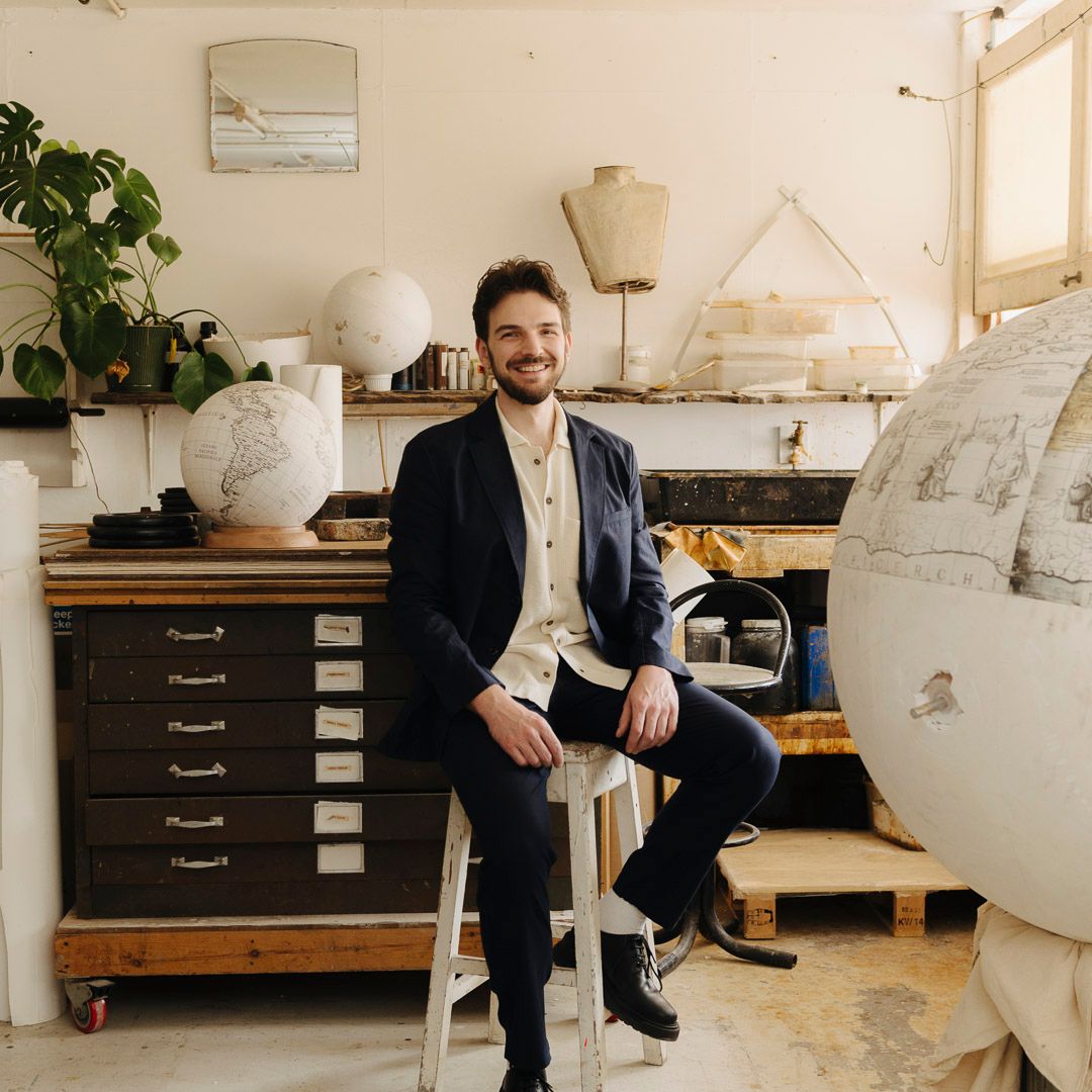 Handcrafting a bespoke globe in a London studio, artisan carefully detailing coastlines and lettering on a vintage-style world map with traditional tools.
