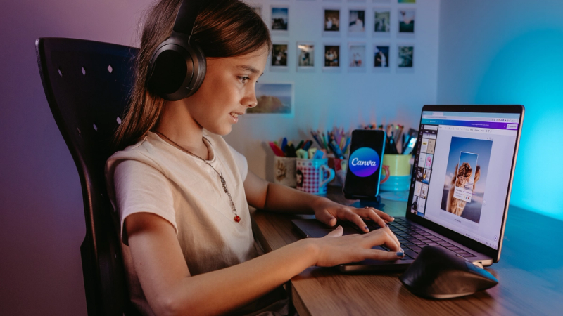 Girl using a laptop with headphones while designing on Canva.