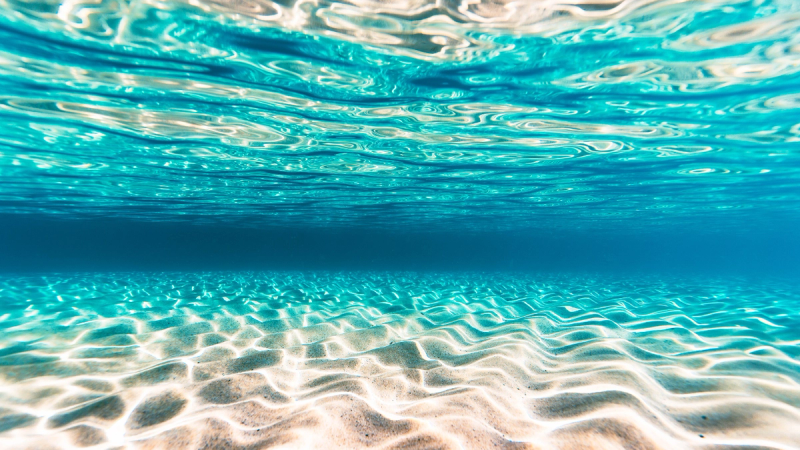 Underwater view of clear blue water and rippled sand.