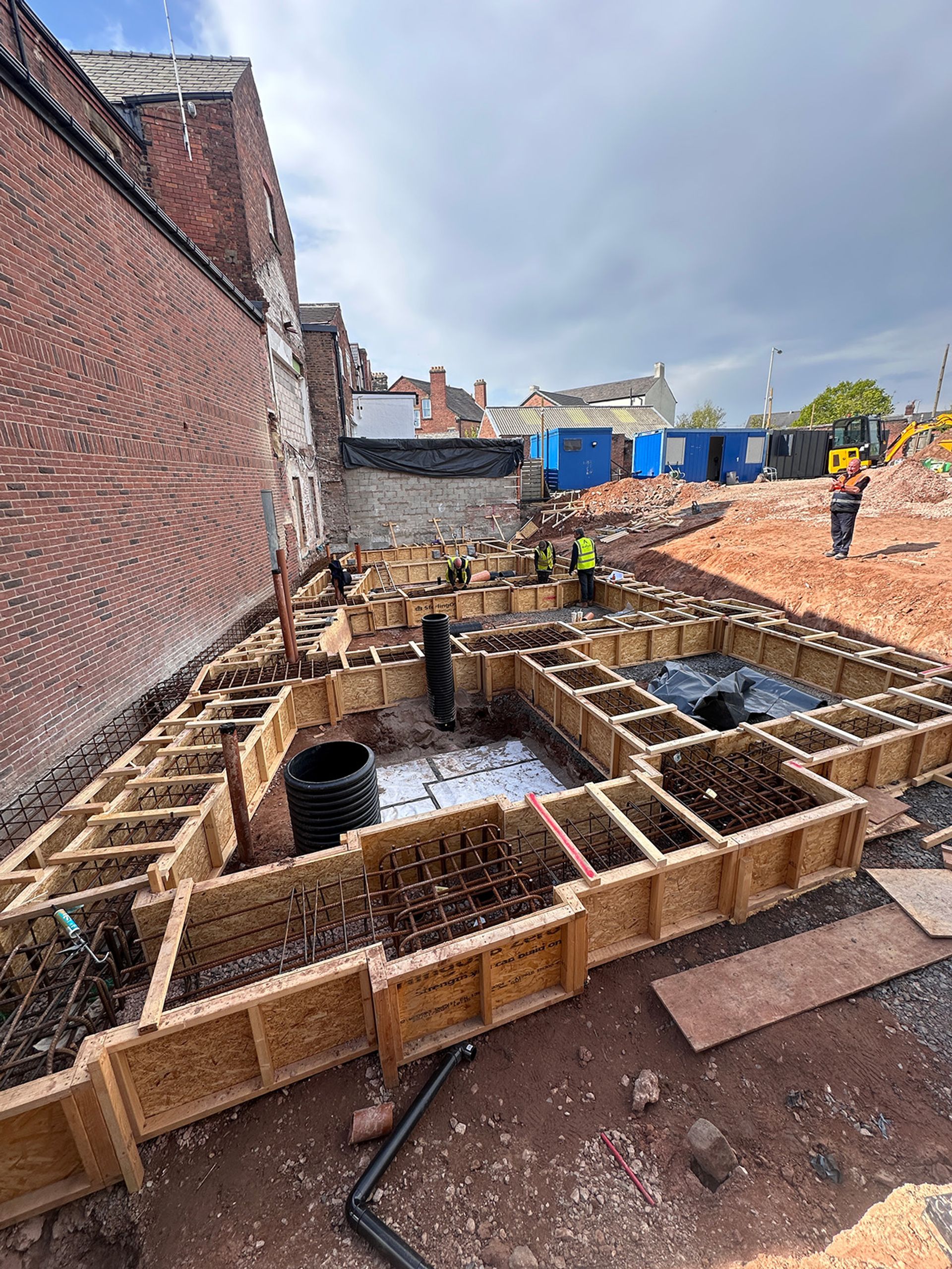 Reinforced concrete foundations being formed against the neighbouring brick wall.