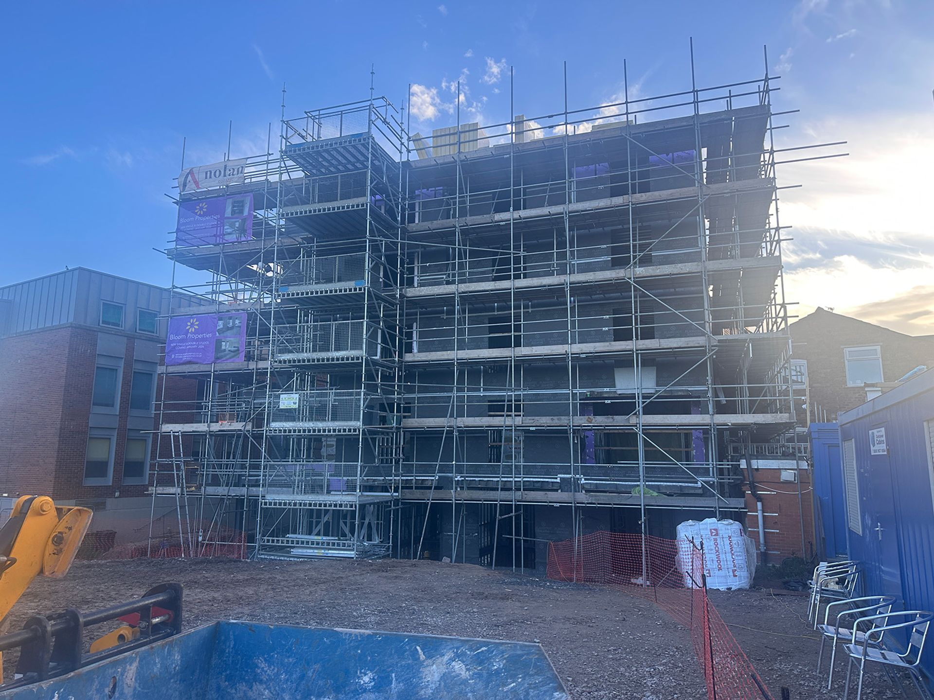 Late afternoon sun behind the scaffolded block, banners fixed to the frame.