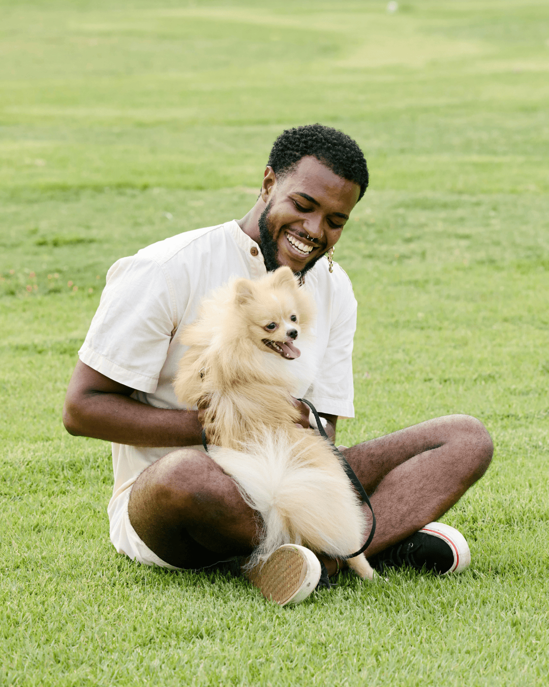 Man happy in park holding onto his small white dog on green grass