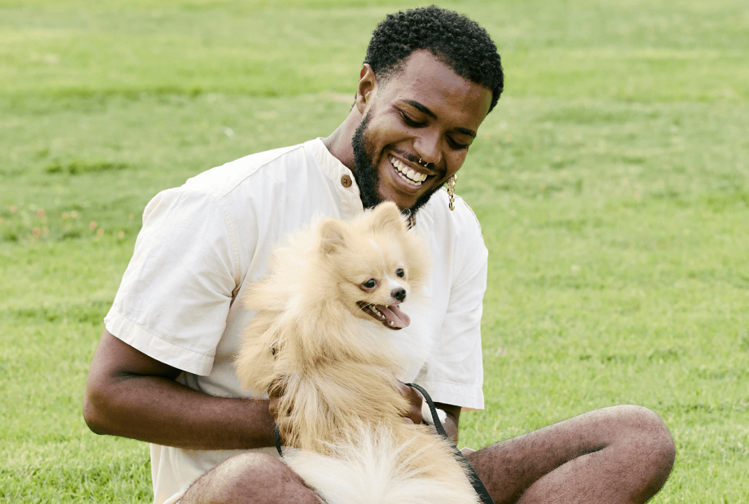 Man happy in park holding onto his small white dog on green grass