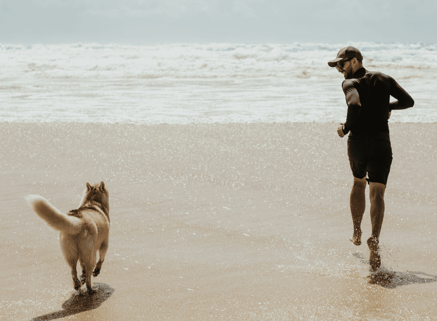 Man running on beach with his husky in the sun