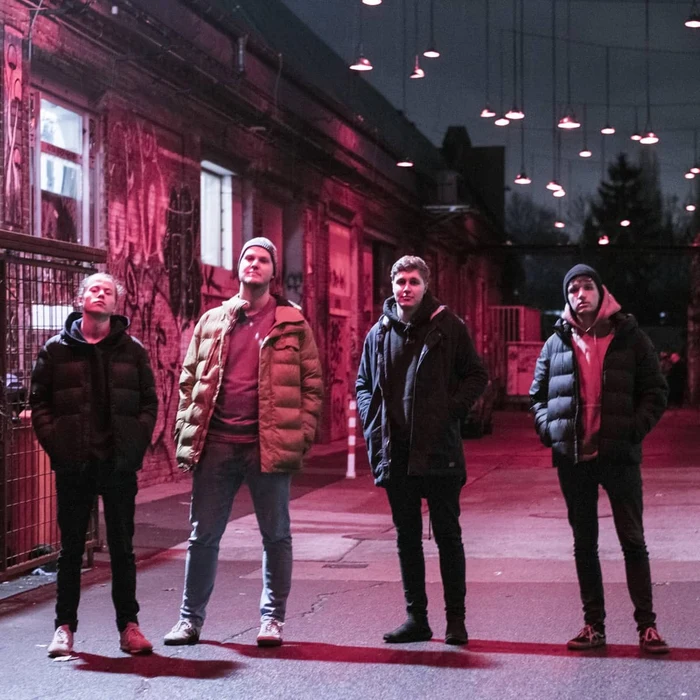 Four young men standing in a redly lit back alley