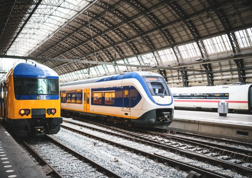 Three passenger trains on tracks under an arched train station roof.