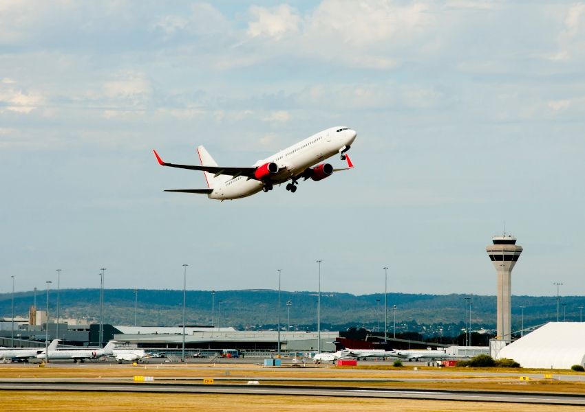 A white airplane with red engines takes off from an airport, with a control tower on the right.