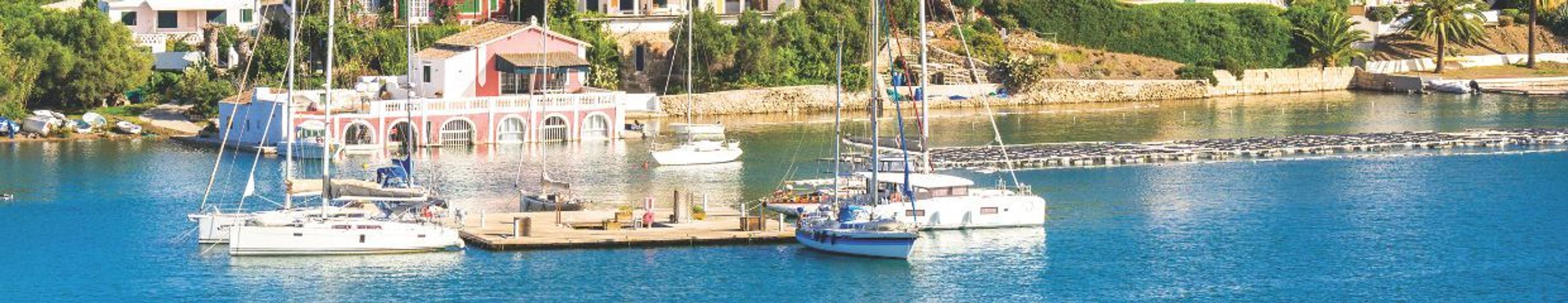 A sunny harbor with blue water, sailboats, and buildings along the shore.