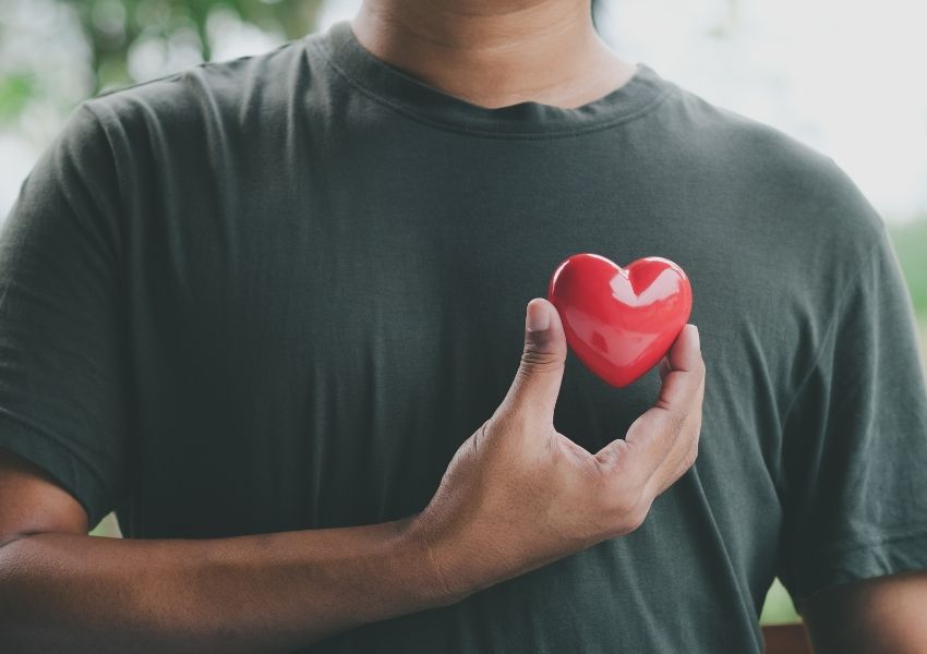 A person in a green t-shirt holding a red heart to their chest.
