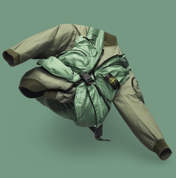 A sage green Stone Island jacket with a shiny emerald green utility vest over it, against a green background.