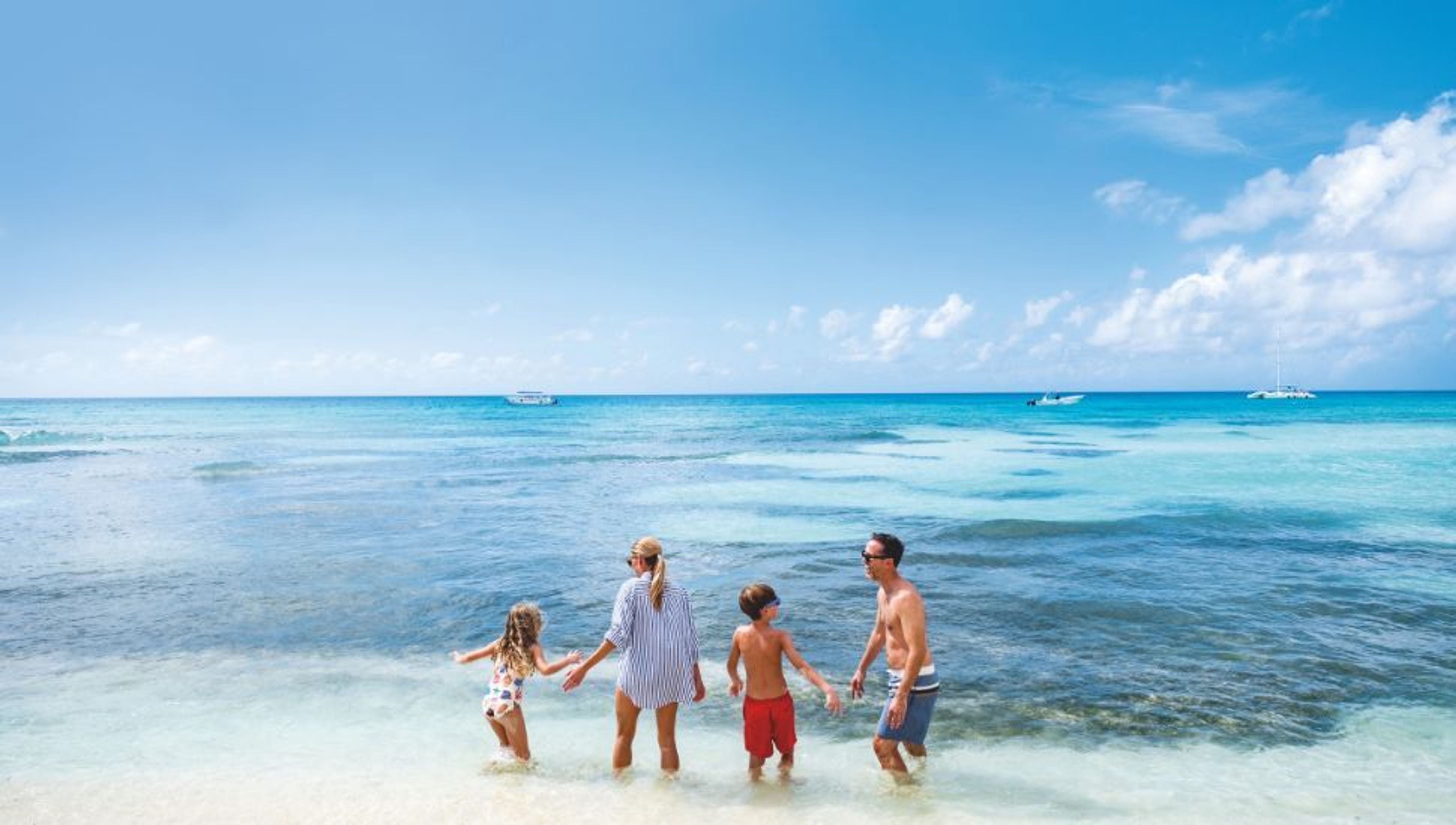 Family of four standing in clear blue ocean water under a sunny sky.