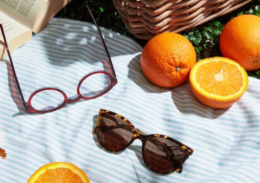 Sunglasses, reading glasses, and oranges on a striped picnic blanket.