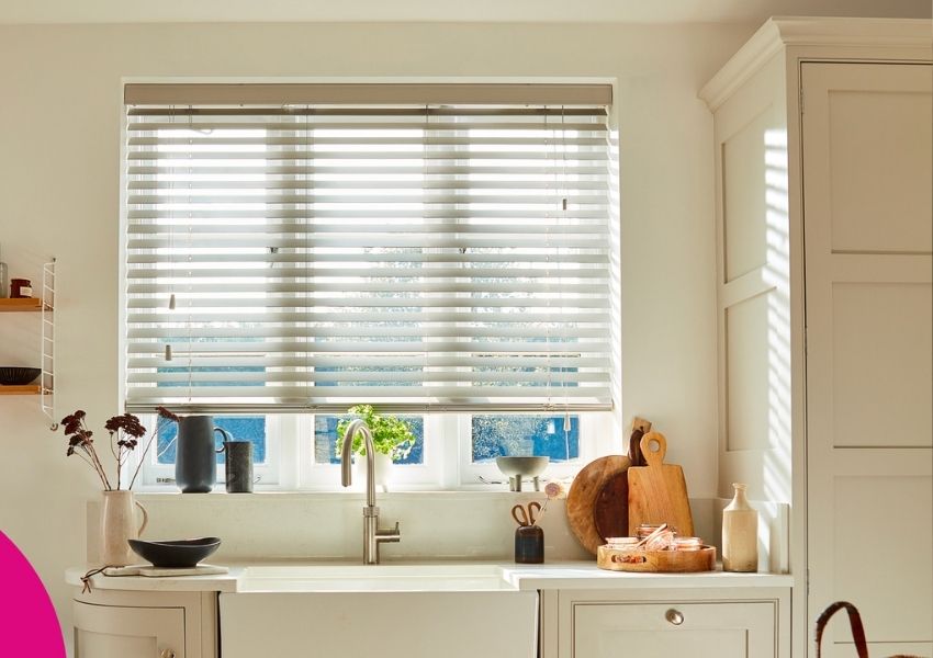 A modern kitchen with a window featuring light grey venetian blinds, a sink, and various decor on the counter.