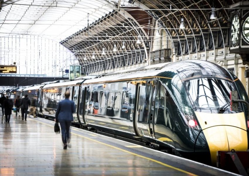 A modern dark green and yellow train stopped at a bustling station platform under an arched ceiling.