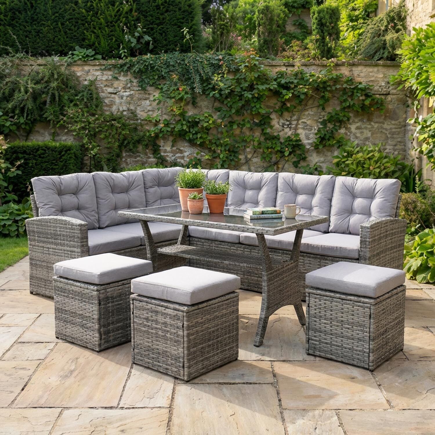 Grey wicker L-shaped outdoor sofa, glass table, and three ottomans with light grey cushions on a stone patio.