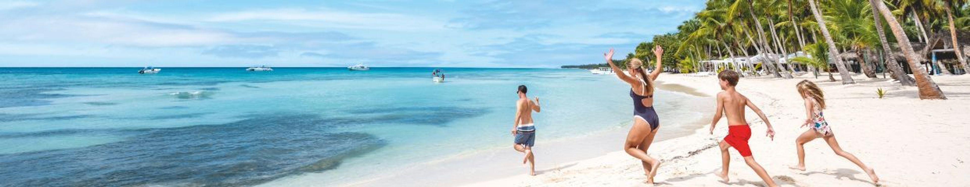 A family runs on a white sand beach towards the turquoise ocean, with palm trees lining the shore.
