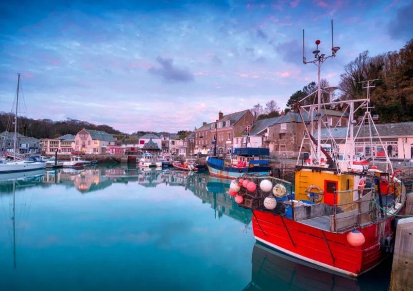 A vibrant harbor at twilight with colorful fishing boats and buildings reflected in the water.