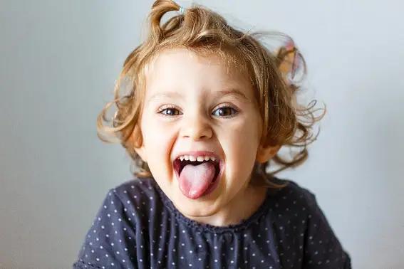 A young child with curly hair sticking out their tongue and laughing.