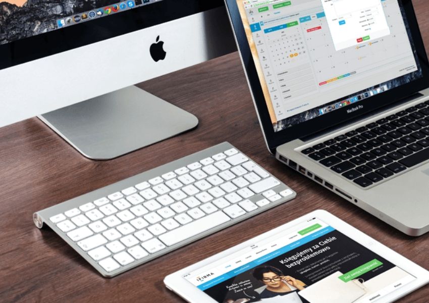 Apple iMac, MacBook Pro, keyboard, and iPad on a wooden desk.